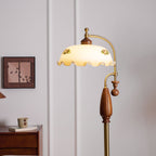 Close view of the frilled floral shade, walnut cap, brass arm and wooden grip, with a framed print behind; a Clérachic floor lamp.
