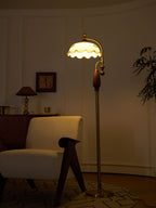 Glowing amber at dusk, the lit frilled shade stands above an armchair and a patterned rug; a Clérachic floor lamp.