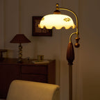 Warm light through the cream glass shade, with a woven table lamp and a sideboard behind; a Clérachic floor lamp.