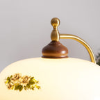 Close view of the brass finial, walnut cap and rose-printed cream glass on the shade of this Clérachic floor lamp.