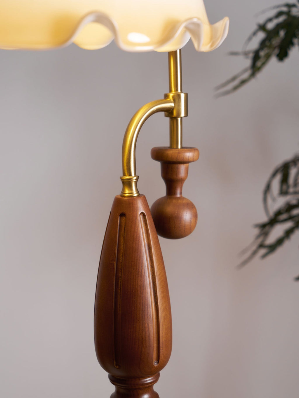 Close view of the walnut-toned grip with its carved flutes, the wooden ball pull and the brass arm, with the shade rim above; Clérachic.