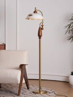 Floor lamp unlit beside a boucle armchair and a pale wall, with a plant at the right edge; a Clérachic design.