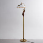 Full-height view of the brass and walnut lamp on a pale grey studio backdrop, with its cord trailing from the base; from Clérachic.