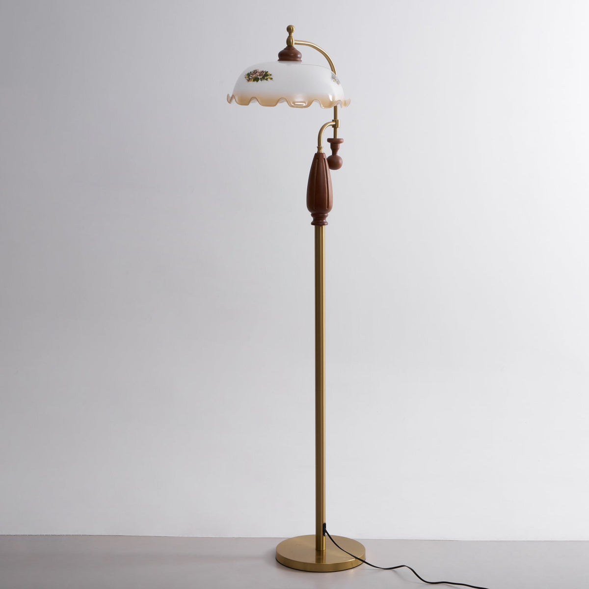 Full-height view of the brass and walnut lamp on a pale grey studio backdrop, with its cord trailing from the base; from Clérachic.