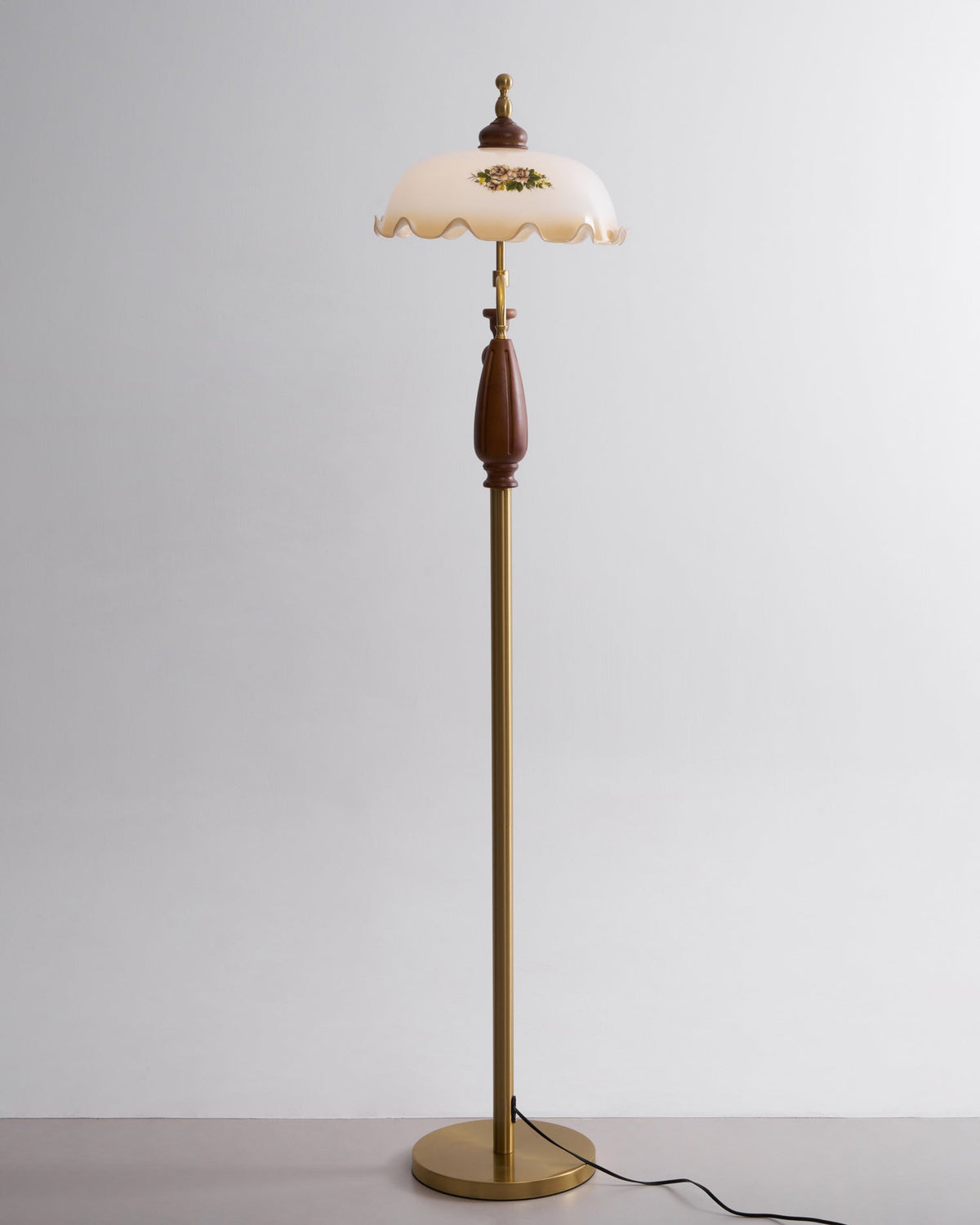 Straight-on studio view of the floral shade at the top of a slim brass stem, against light grey; a Clérachic floor lamp.