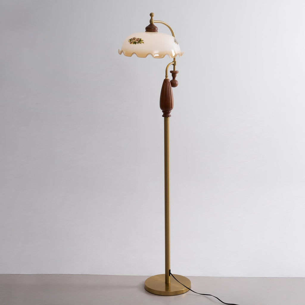 Three-quarter studio view of the walnut grip, the brass stem and the round base, in front of a plain grey wall; a Clérachic floor lamp.