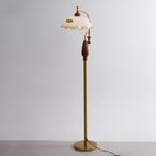 Three-quarter studio view of the walnut grip, the brass stem and the round base, in front of a plain grey wall; a Clérachic floor lamp.