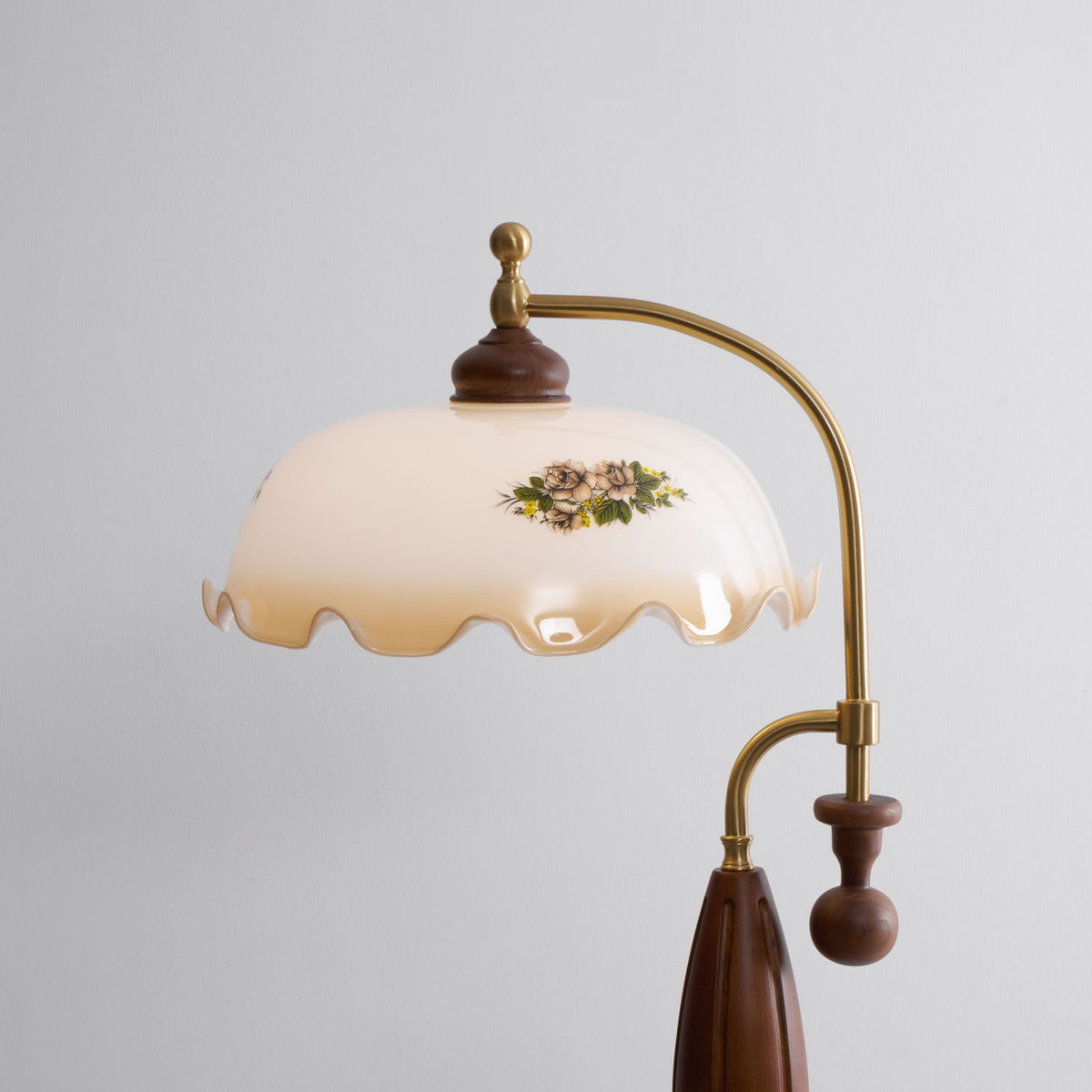 Close studio view of the wide, wavy-edged glass shade with its small rose print and the brass arm; this Clérachic floor lamp.