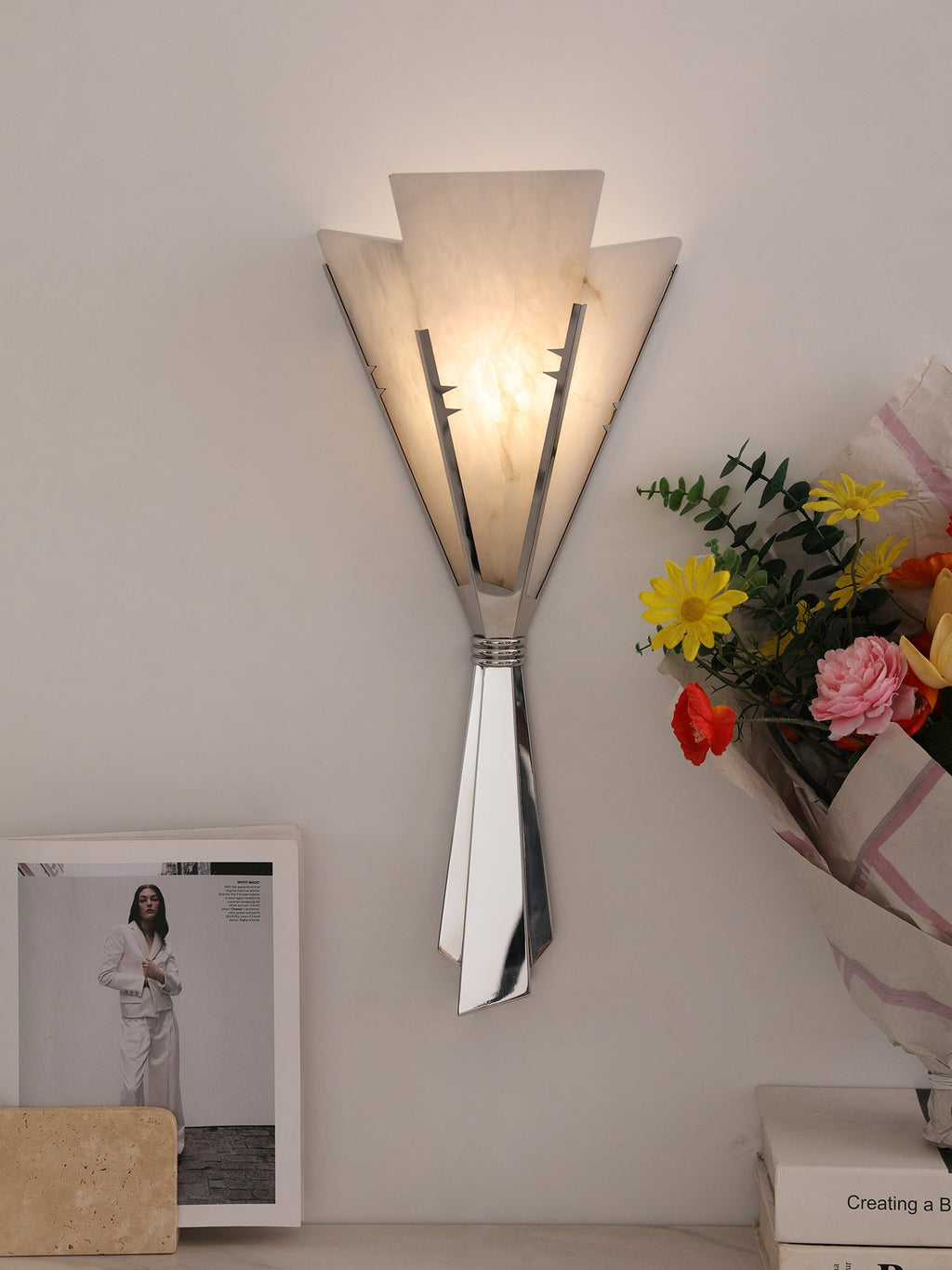 Clérachic Florent sconce lit on a pale wall beside a bouquet and a framed print.
