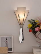 Clérachic Florent sconce lit on a pale wall beside a bouquet and a framed print.