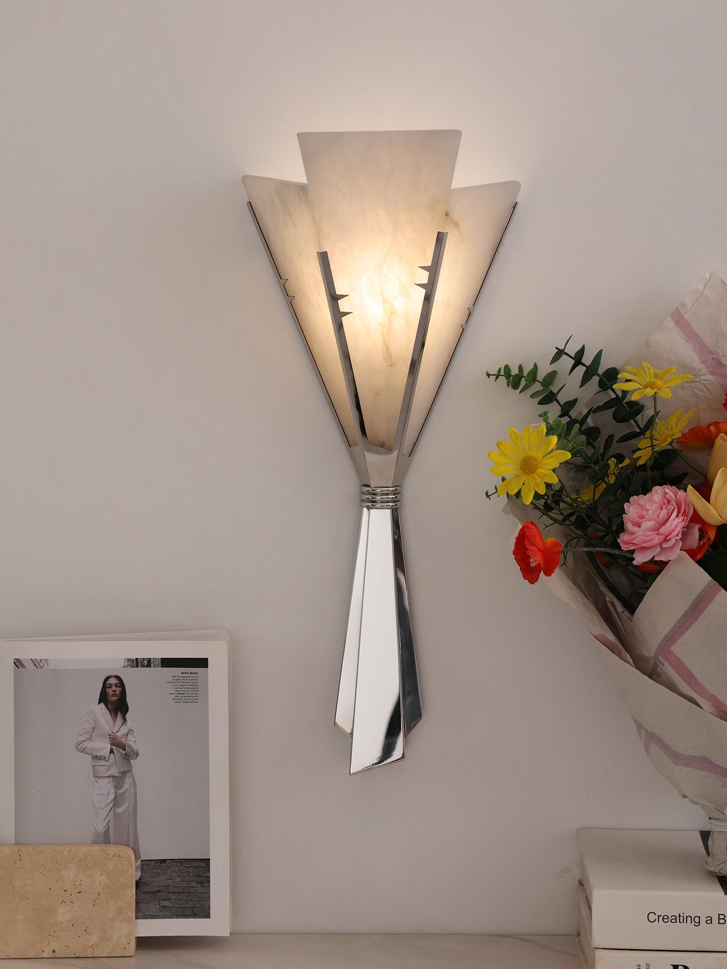 Clérachic Florent sconce lit on a pale wall beside a bouquet and a framed print.