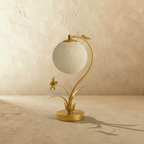 Clérachic gold table lamp switched off, a textured woven off-white sphere hanging from a curved stem with a metal flower.