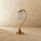 Clérachic gold table lamp switched off, a smooth frosted white sphere hung from a curved stem with a small flower.