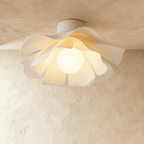 Clérachic white acrylic ceiling light with a wavy petal-like shade and a glowing round bulb, lit against a limewash ceiling.