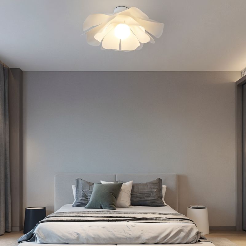 Clérachic white petal-shade ceiling light lit above a low platform bed in a calm grey bedroom with layered cushions.