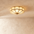 Clérachic scalloped flush ceiling light with frosted glass panels and brass-toned ribs, glowing warm on a limewashed ceiling.