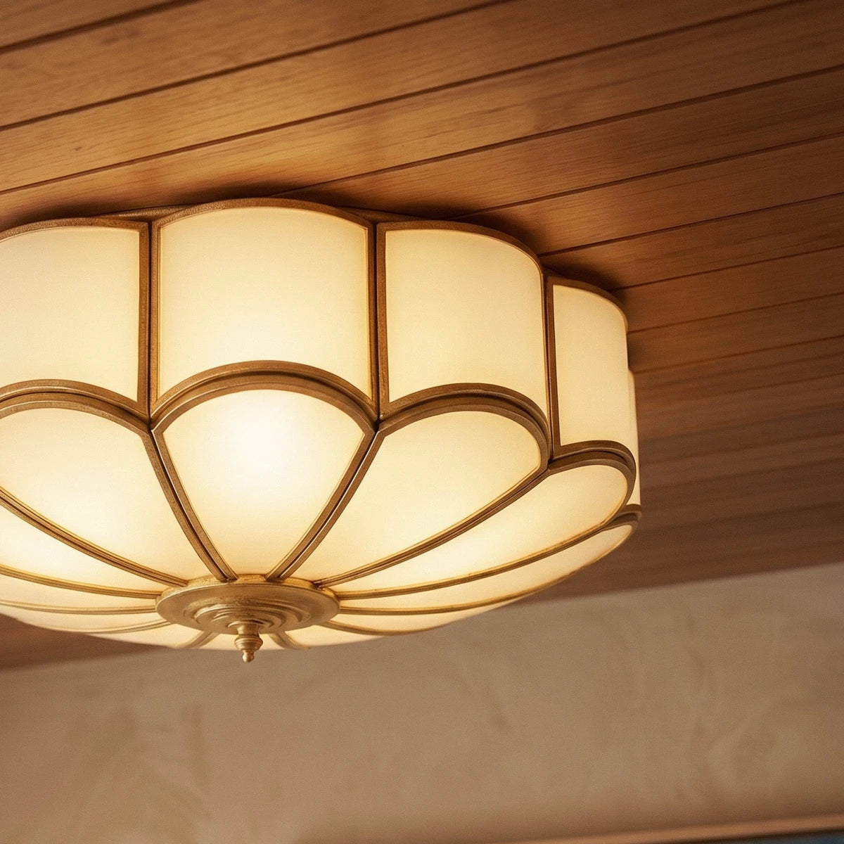 Clérachic scalloped flush ceiling light seen from below, frosted glass panels in brass-toned ribs on a timber ceiling.