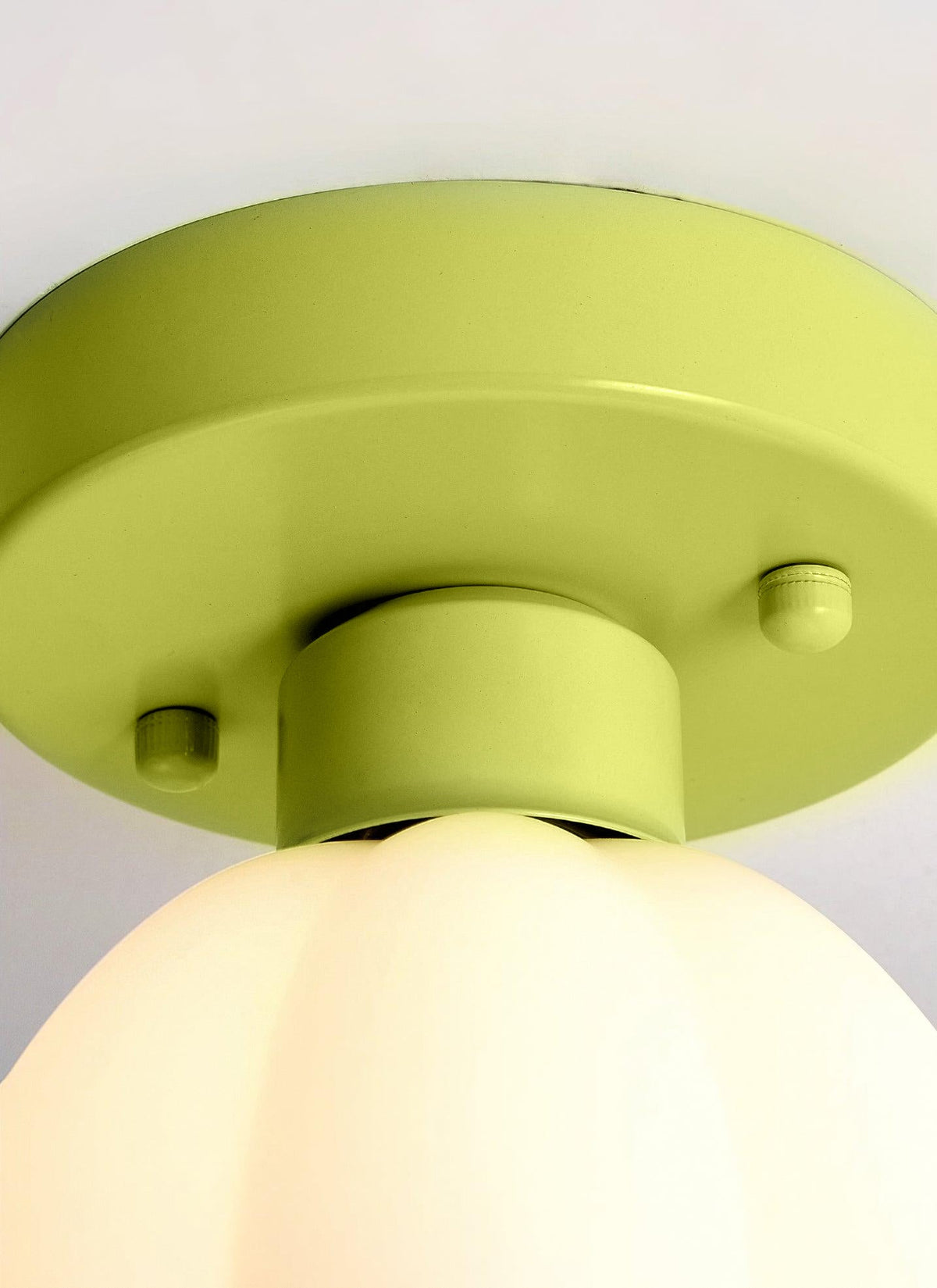 Close view of the green canopy and fixing screws of this Clérachic light, with the top of its white glass shade glowing below.