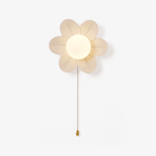 Six-petal white flower wall light from Clérachic, lit around a round opal globe, with a gold chain and pull on a plain white backdrop.