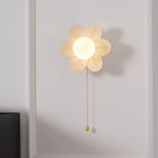 Close view of the white resin petals and glowing globe of this Clérachic wall light, with its pull chain hanging below.