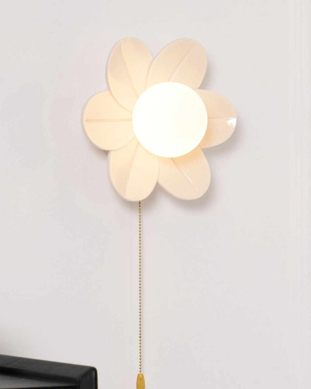 Large close crop of the six sculpted petals and lit globe on this Clérachic flower wall light, with a long gold chain below.