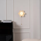 Flower wall light from Clérachic glowing gently on a white panelled wall, above a black cabinet and a pair of magazines.
