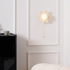 Lit petal sconce from Clérachic on a white panelled wall, with a coffee cup on the black cabinet and a cream sofa edge in view.