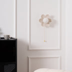 This Clérachic flower wall light switched off, its petals and round white globe plain against a panelled wall above a black cabinet.
