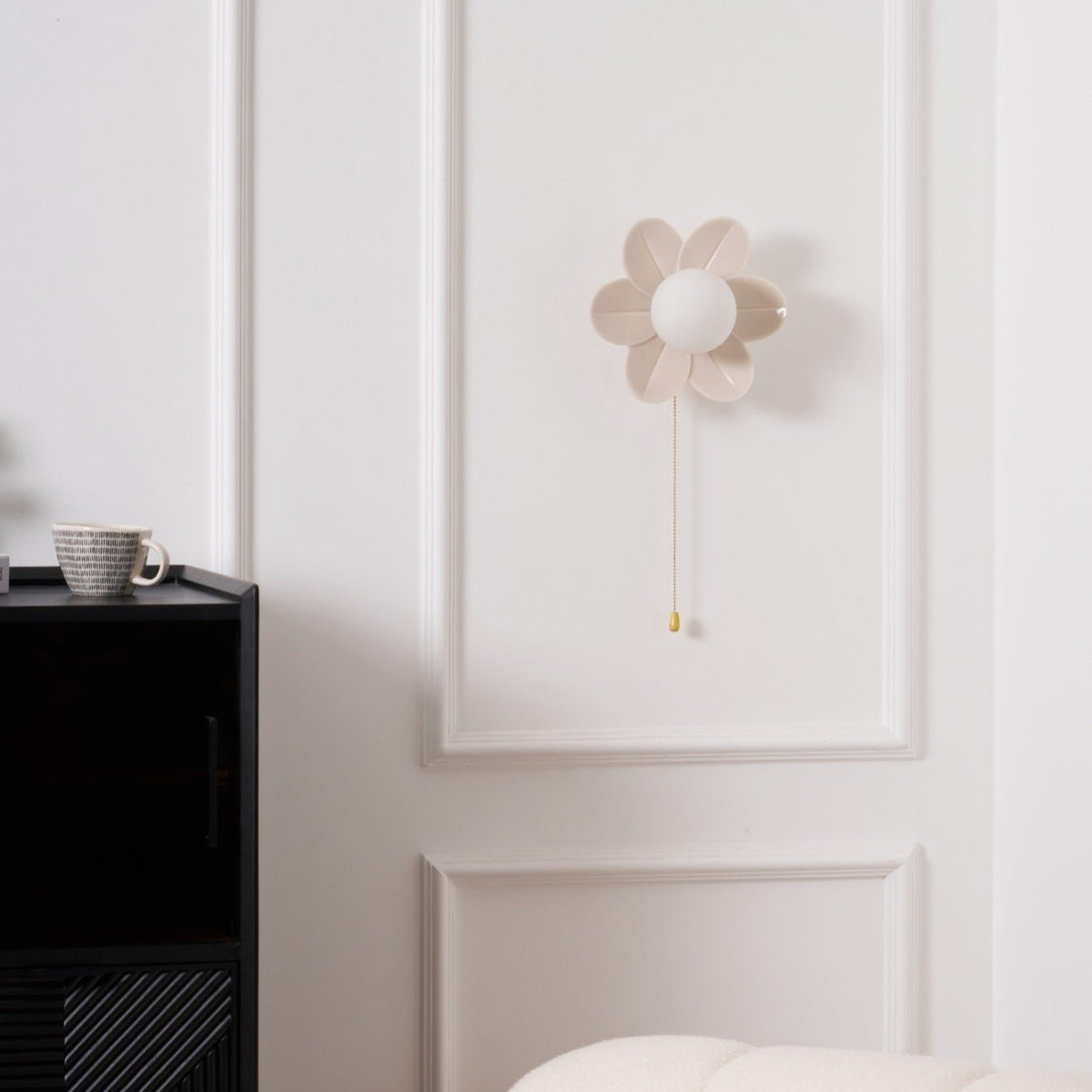 This Clérachic flower wall light switched off, its petals and round white globe plain against a panelled wall above a black cabinet.