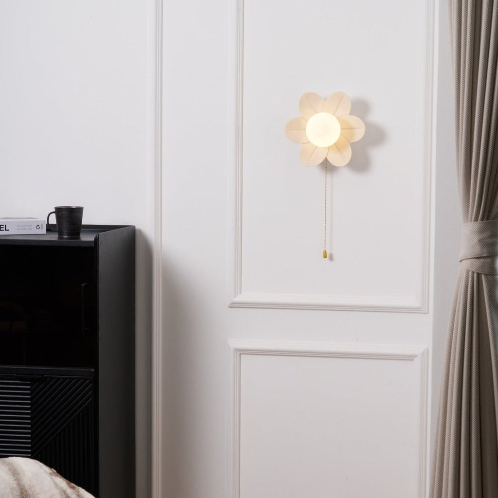 Clérachic flower wall light lit above a black cabinet with a mug on top, a heavy curtain hanging at the right edge of the wall.