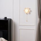 Clérachic flower wall light lit above a black cabinet with a mug on top, a heavy curtain hanging at the right edge of the wall.