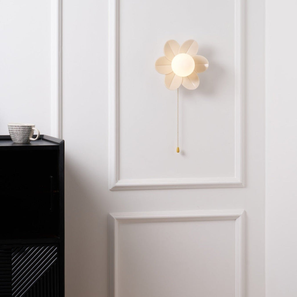 Switched-on flower sconce from Clérachic on a white moulded wall, with a mug resting on the black cabinet at lower left.