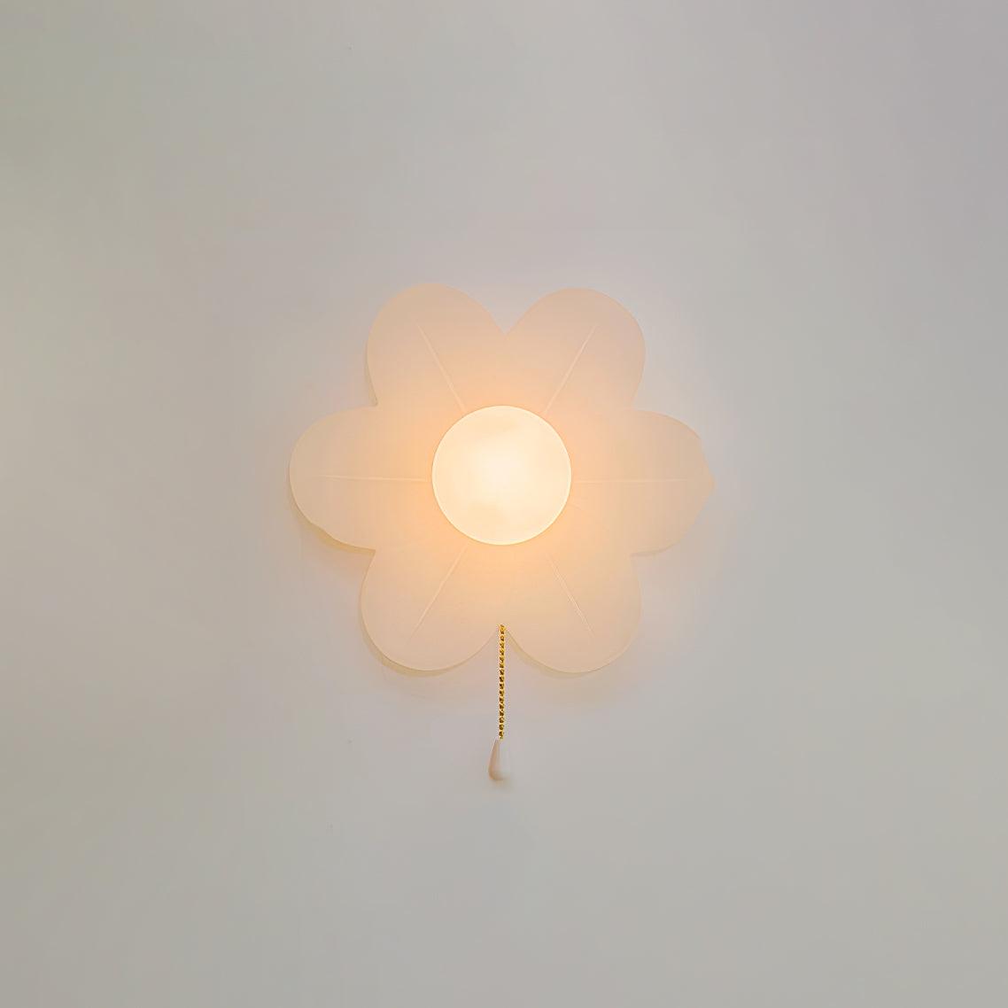 Softly lit white flower wall light on a pale grey wall, this Clérachic sconce showing warm light through its frosted petals.