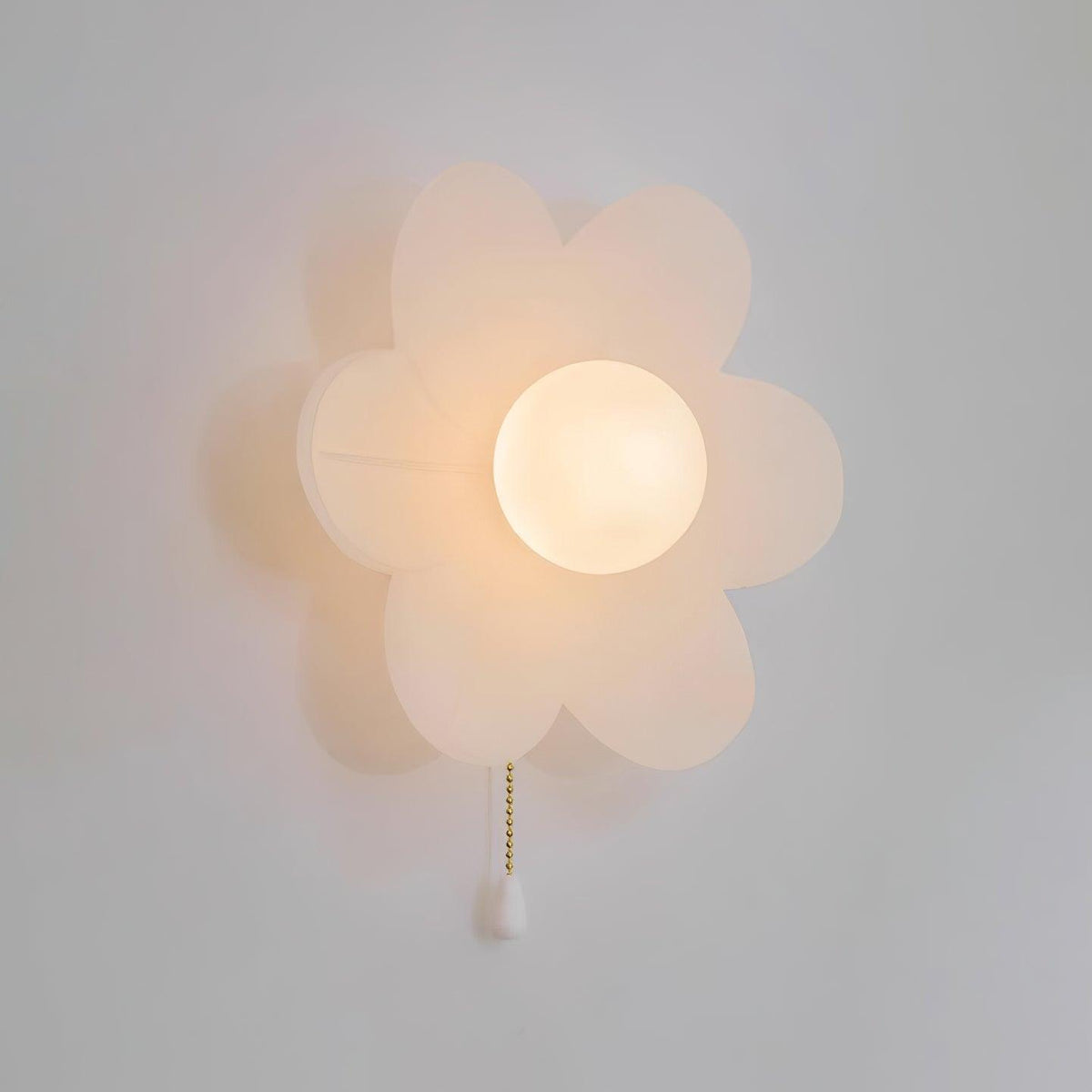 Close, warm-lit view of the rounded white petals around a frosted globe on this Clérachic wall light, with a white pull on the chain.