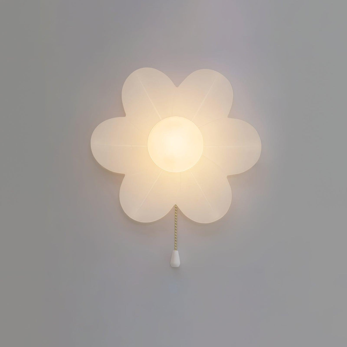 Glowing flower-shaped Clérachic wall light on a grey wall, its petals softly translucent and a white pull at the end of the chain.