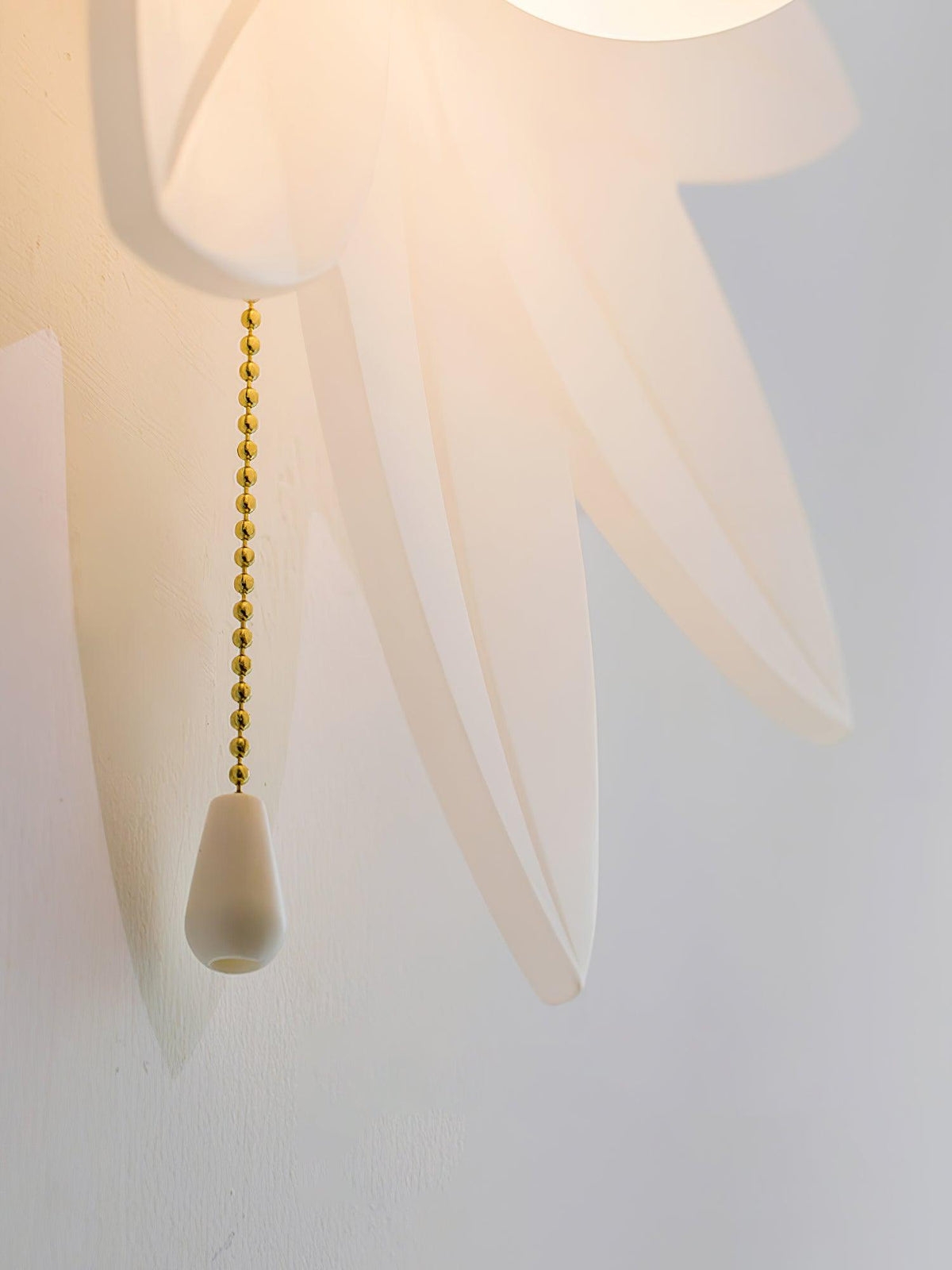 Detail of the translucent petal tips and the gold bead chain with a white pull on this Clérachic flower wall light.