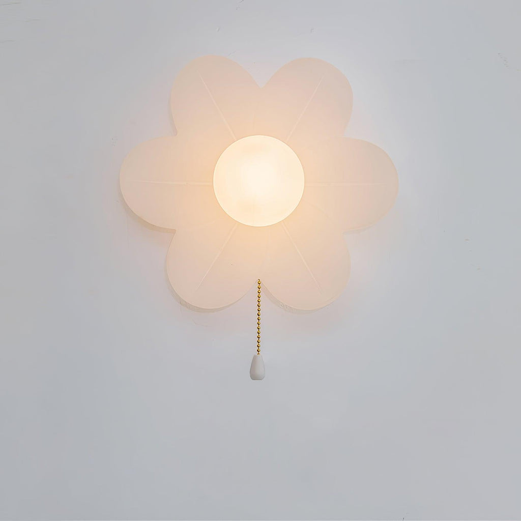 Frosted-white Clérachic flower sconce lit warmly on a pale wall, with a dainty gold chain ending in a white pull.