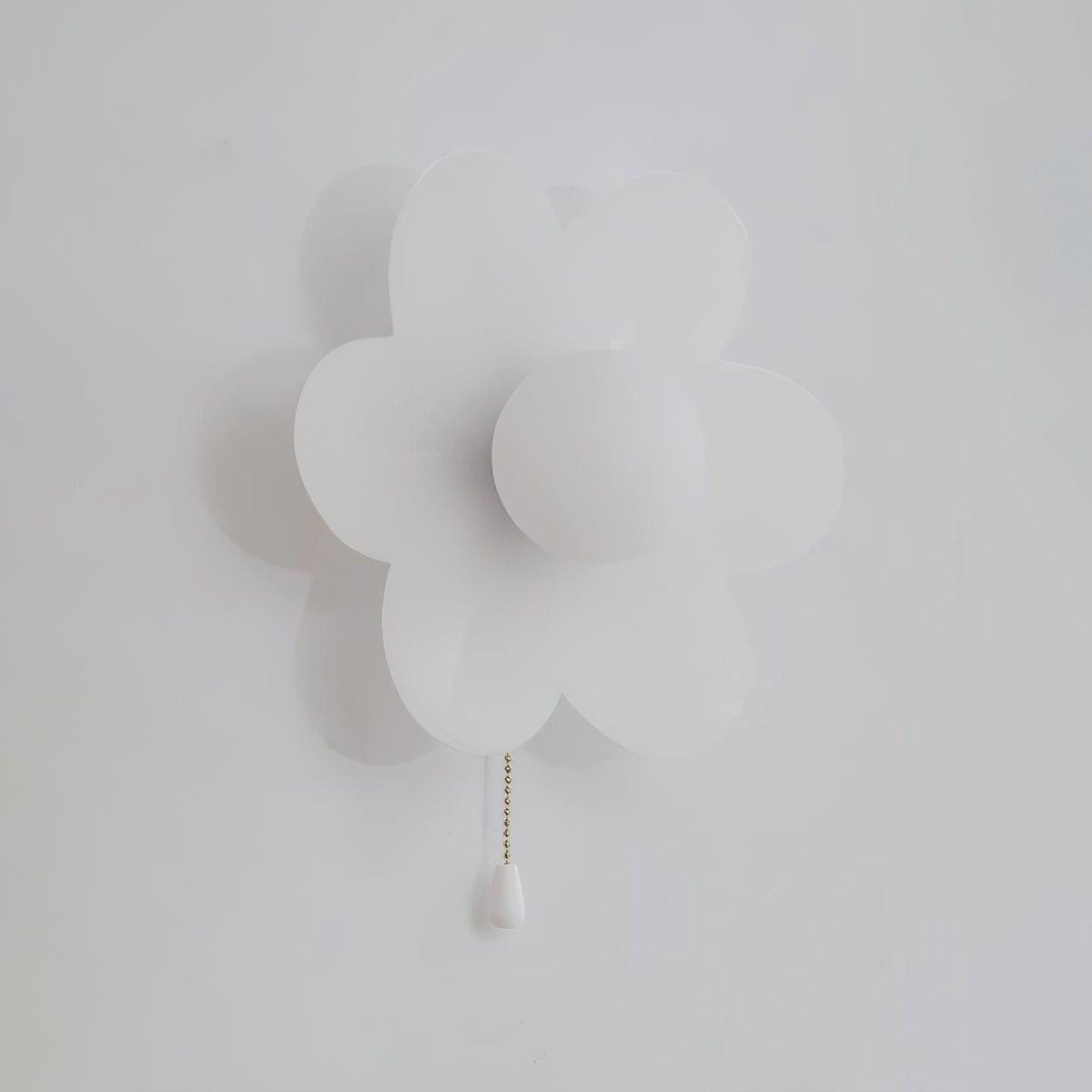 Unlit white Clérachic flower wall light on a pale grey wall, with a flat round globe at the centre and a white chain pull.