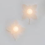 Two lit wall lights from Clérachic with pointed, star-like petals on a pale wall, each with a small pull chain.