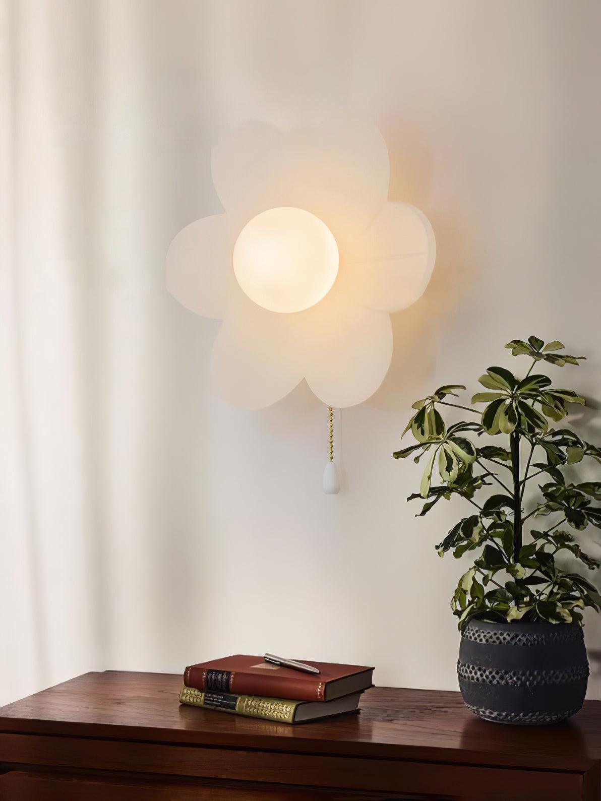 Clérachic flower wall light beside a curtain above a walnut sideboard, with a potted plant and two books on the wood surface.