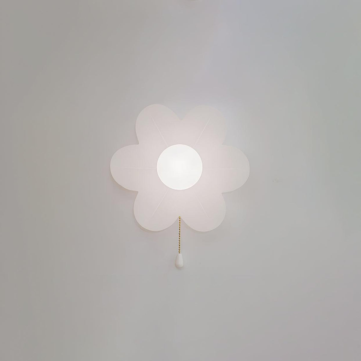 A Clérachic flower wall light with a soft pearly glow on a grey wall, its petals gently translucent and a white pull on the chain.