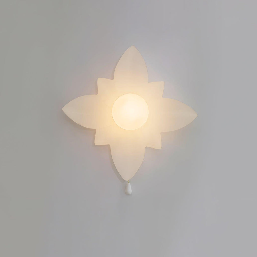 Four-point star-shaped Clérachic wall light lit warmly on a grey wall, with a frosted globe at the centre and a white pull below.