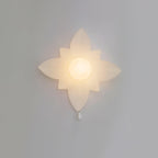 Four-point star-shaped Clérachic wall light lit warmly on a grey wall, with a frosted globe at the centre and a white pull below.