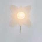 A larger four-point petal wall light from Clérachic with a lit globe and a gold chain, on a pale wall.