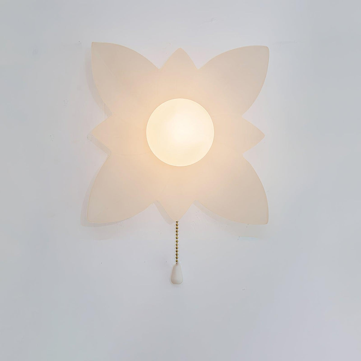 A larger four-point petal wall light from Clérachic with a lit globe and a gold chain, on a pale wall.