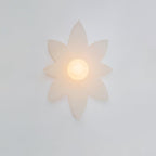 Eight-point petal wall light from Clérachic glowing on a pale wall, with a frosted globe and no chain pull in view.