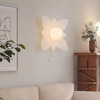 Four-point petal Clérachic wall light on a cream wall beside a walnut shelf, a plant and a corner of a cream sofa.