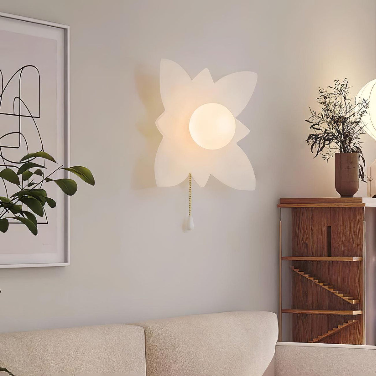 Four-point petal Clérachic wall light on a cream wall beside a walnut shelf, a plant and a corner of a cream sofa.