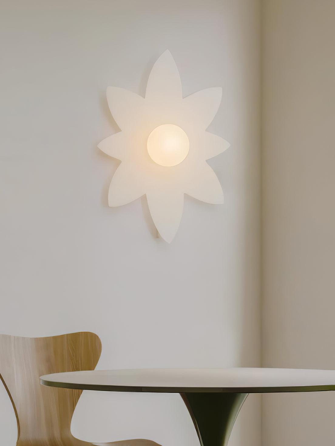 Eight-point petal Clérachic wall light on a wall above a table with a wooden chair, in a calm neutral room.