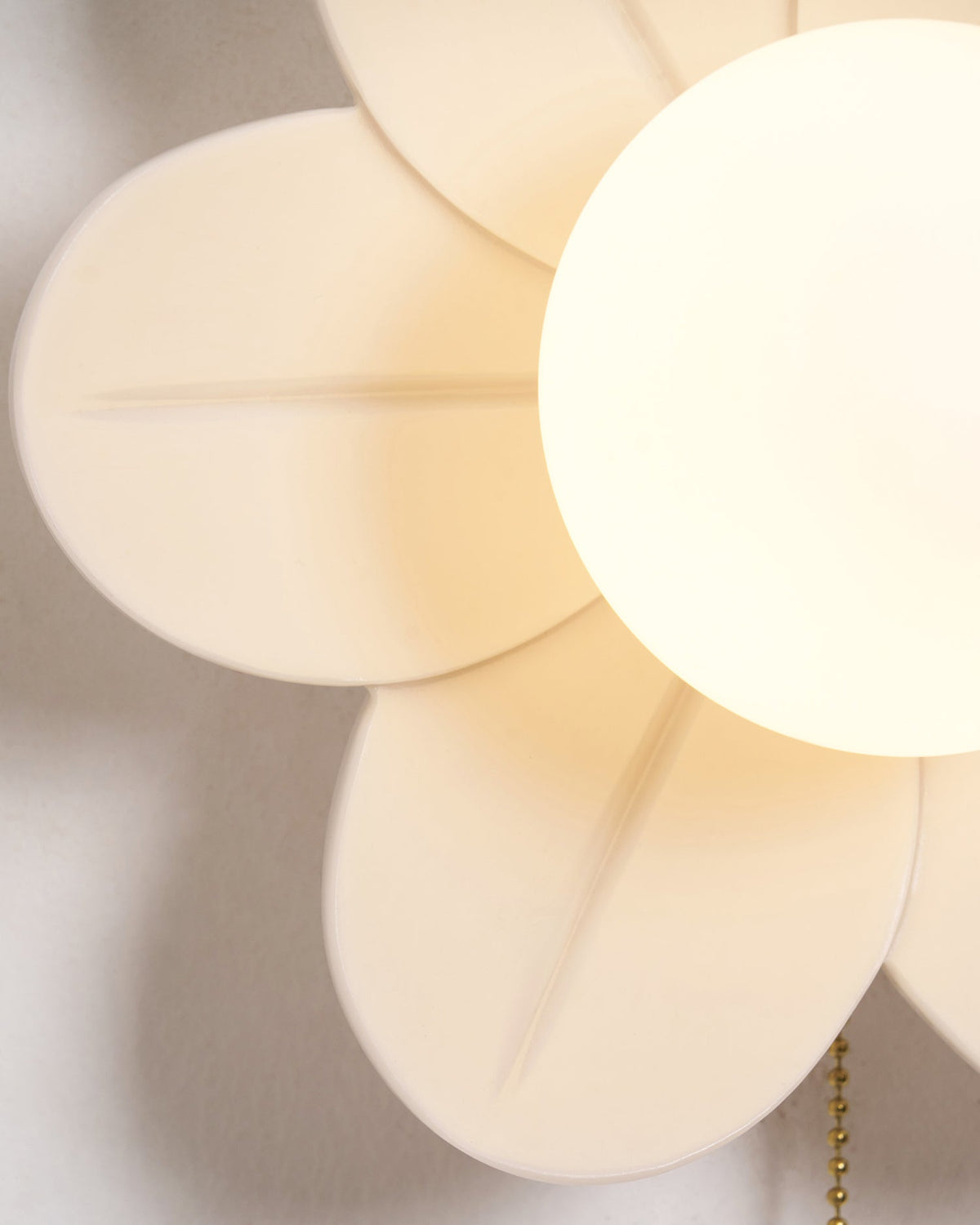 Soft-focus close-up of the petals, central globe and chain of this Clérachic flower wall light, lit from within.